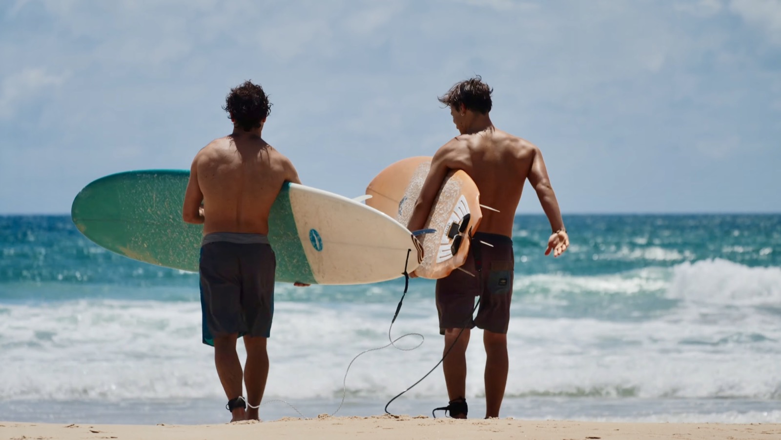 Giacomo and Isaac carrying their surfboards toward the ocean together